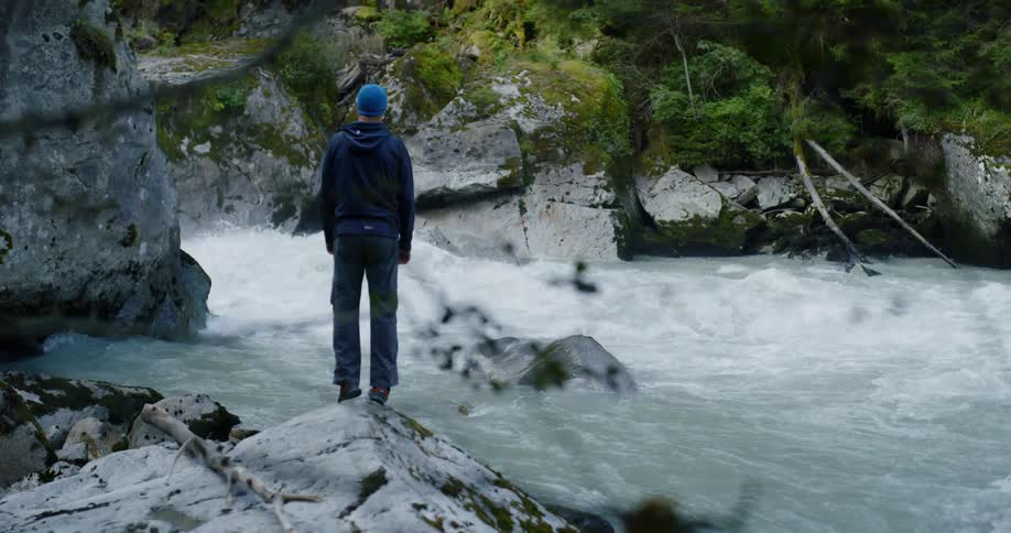 Man standing on a rock next to river rapids