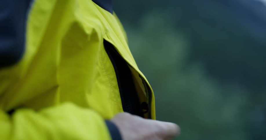 A person pulls something out of a jacket pocket and zips it up
