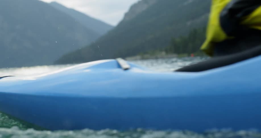 Person paddling in a blue kayak on the river in the mountains