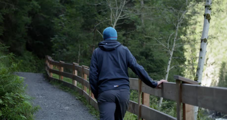 A person is weary after a long hike and slows their pace by touching the wooden guide rail on the trail