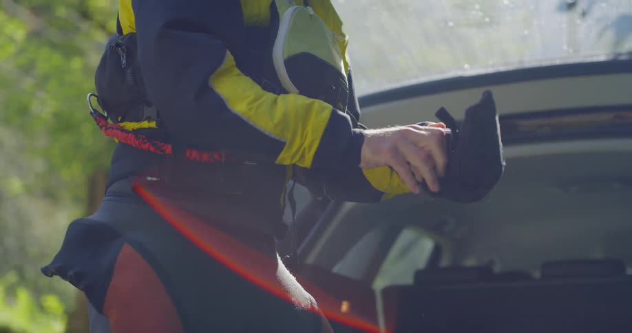 A person puts on gloves near the back of a car