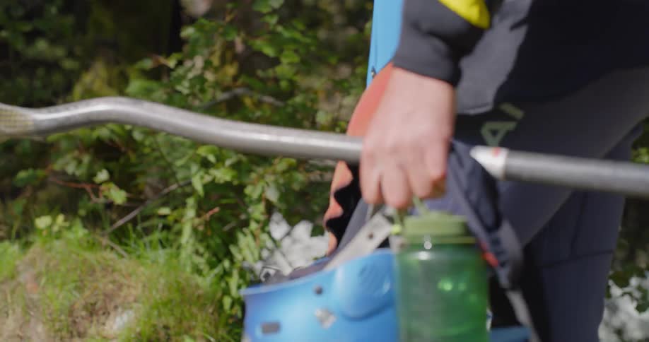 A person walks along carrying a paddle helmet and water bottle