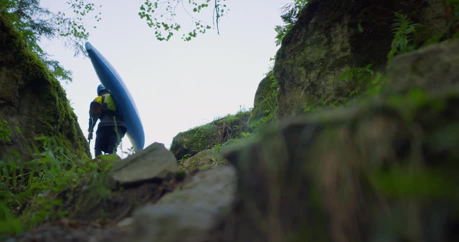 Person carrying a canoe walking over rocks through the mountains
