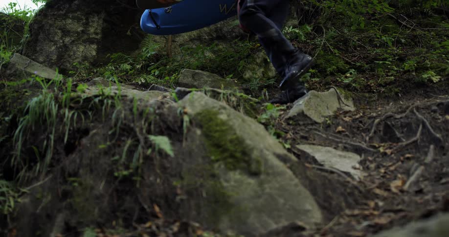 A person holding a kayak and paddle walks across a rocky ledge