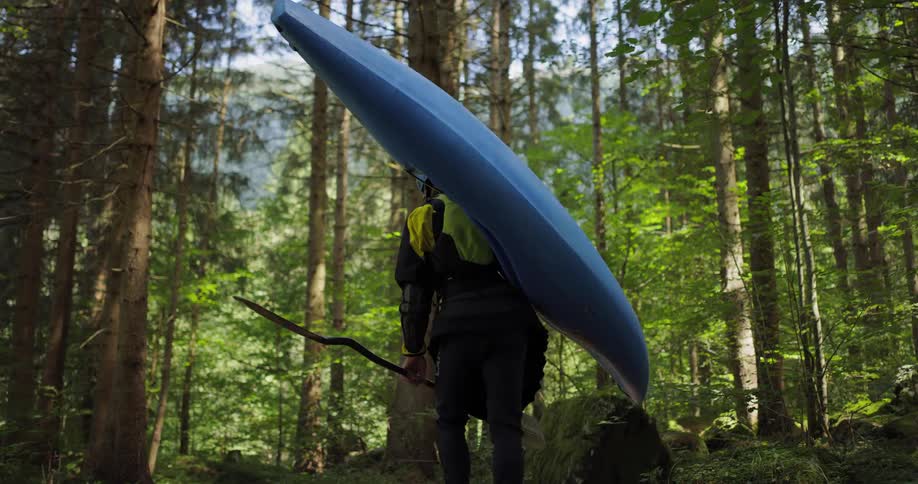 A person carries a kayak through the forest