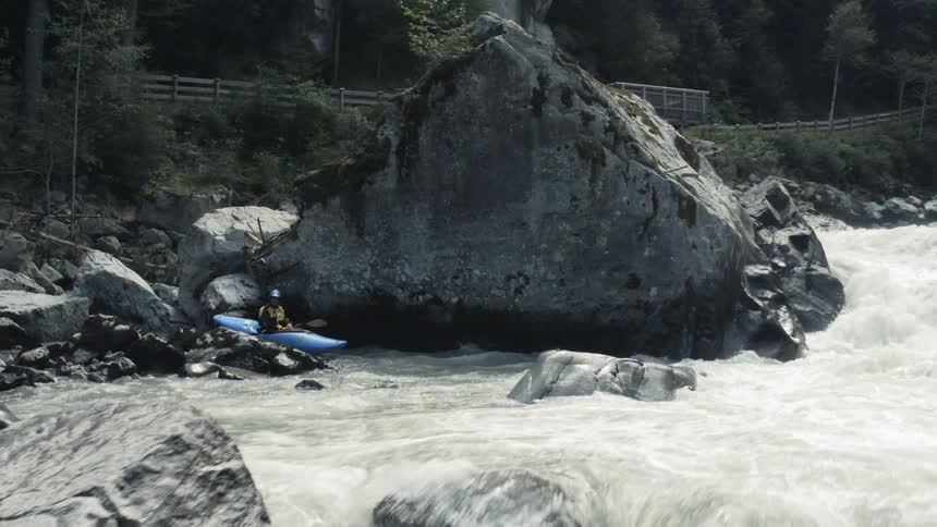 A kayaker sits in calm waters watching boiling rapids