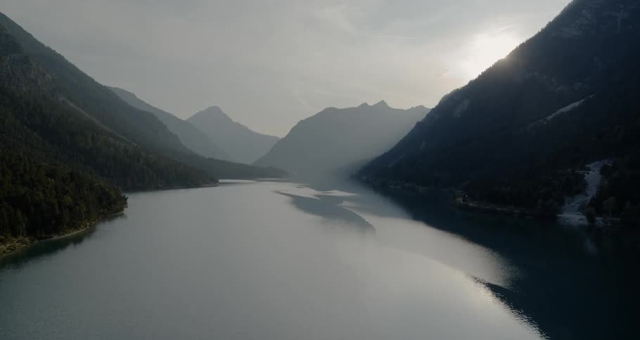 A lake running through mountains and forest with a rising sun
