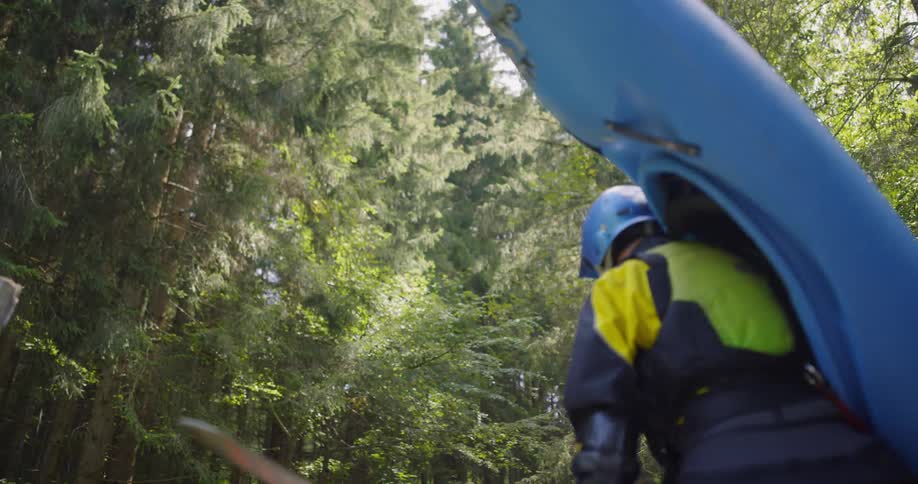A person carries a kayak and a paddle through the forest
