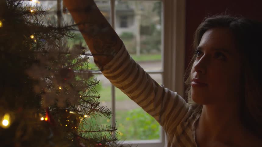 A woman hanging christmas ornaments from a tree
