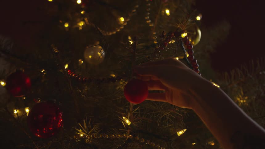 A person hangs a bulb on a christmas tree