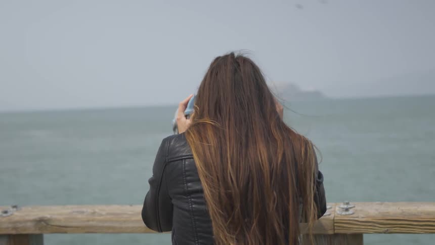 A brunette female looks out of binoculars on the coast on a windy day