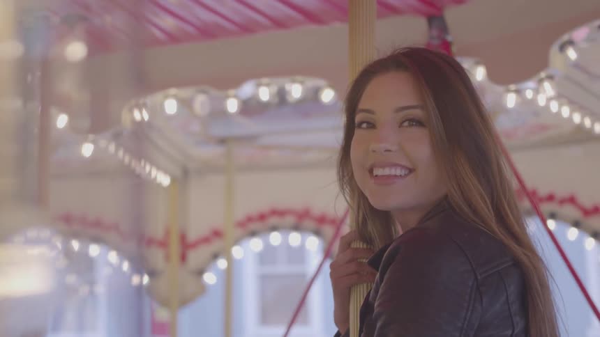 A woman looks at the camera and smiles while riding a carousel