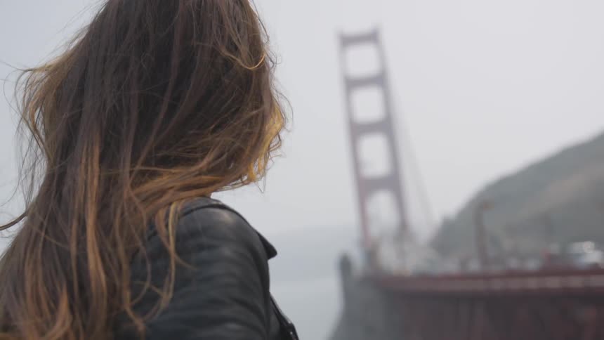 Woman stands next to and looks out towards the golden gate bridge