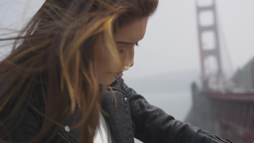A brunette females hair blows in the wind while the golden gate bridge is in the background