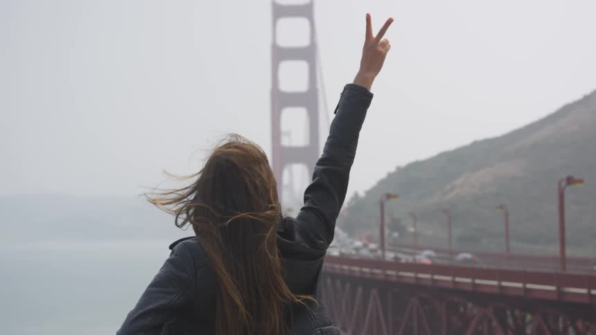 A woman flashes the peace sign at the golden gate bridge