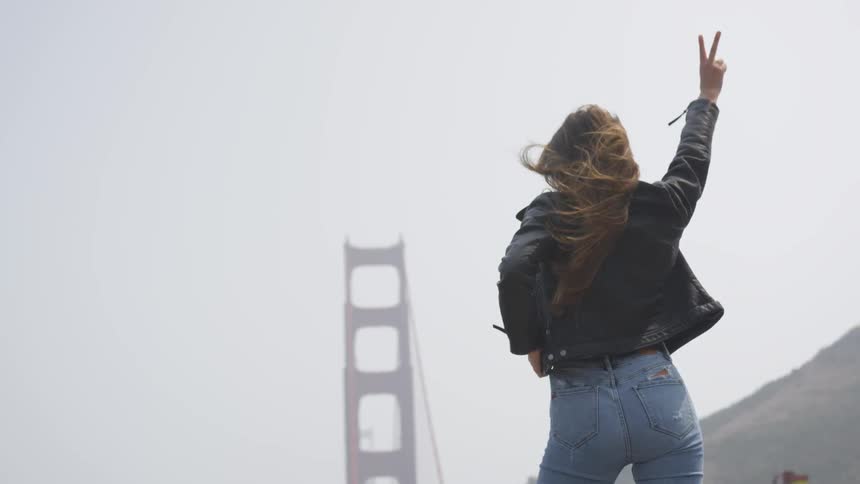 A woman with a leather jacket and jeans with a bridge in the background