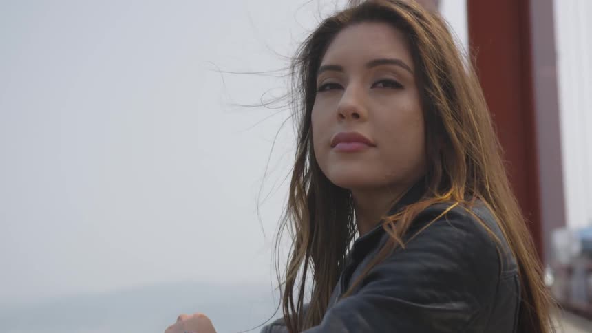 A hispanic woman looks over the side of a bridge and then looks away