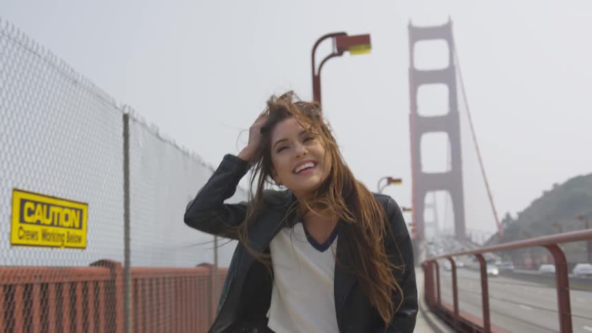 A woman runs on the pedestrian path of the golden gate bridge her long hair bouncing and she turns and smiles and laughs