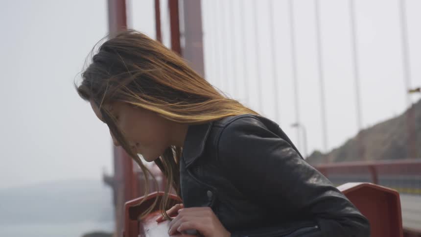 A woman looks over the side of a large bridge while cars drive passed