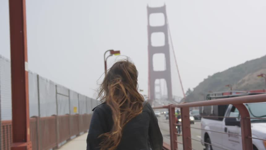 A laughing woman waves and turns and continues to skip and walk on the golden gate bridges pedestrian path