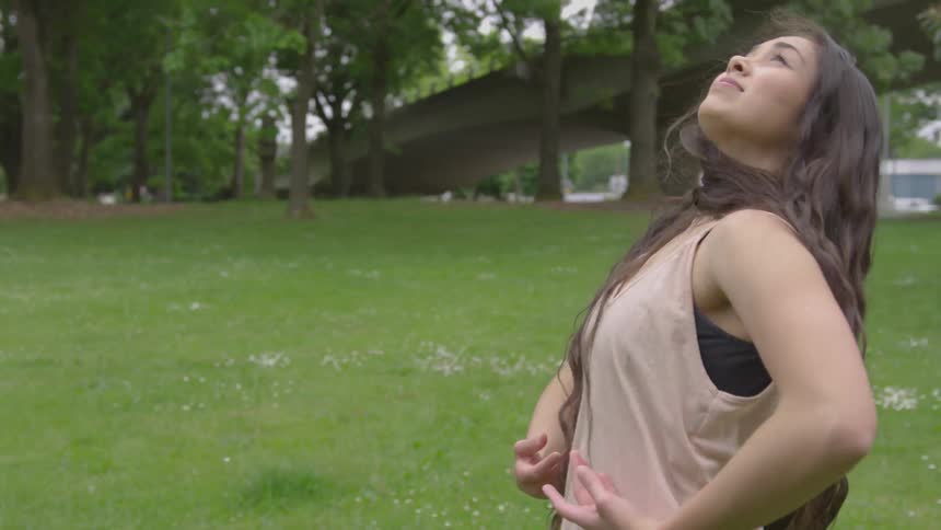 A woman dances in the grass in a park