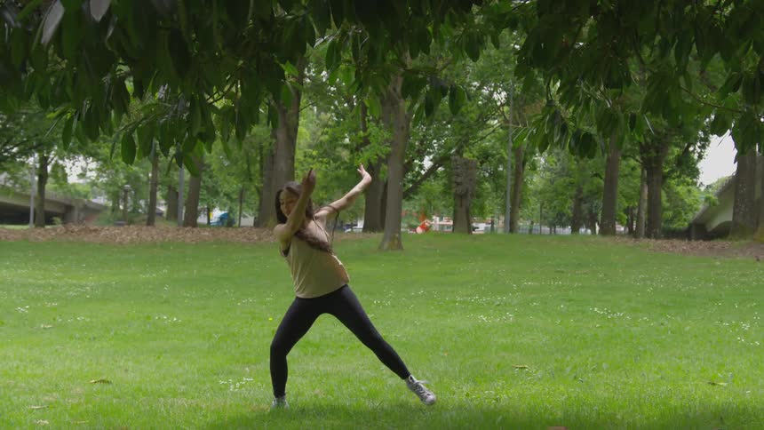 A woman in yoga pants dances on green grass in a park