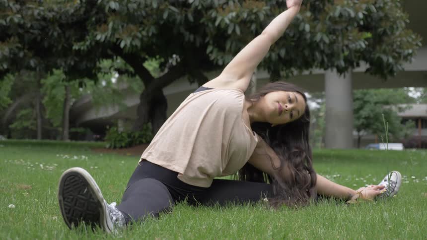 A woman stretches on a grassy lawn in a park