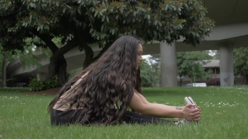 A woman stretches while sitting in the grass