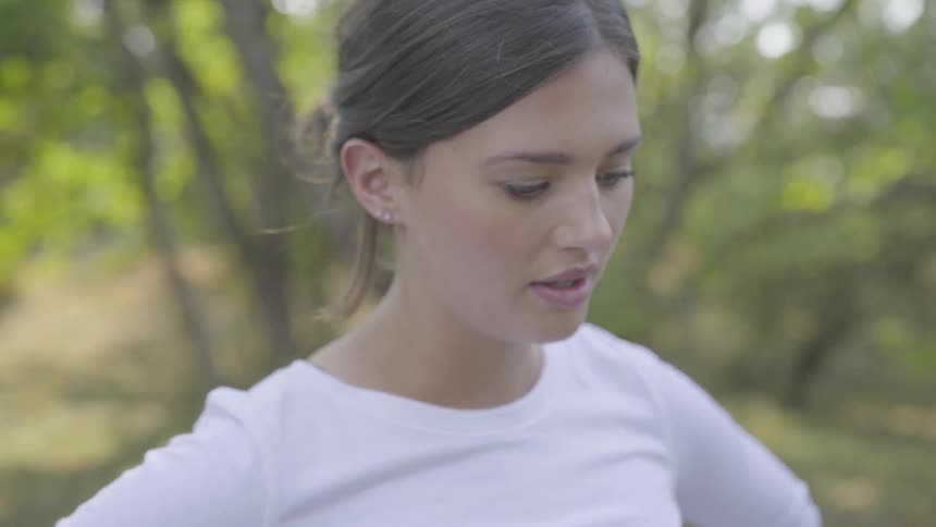 A young brunette woman with her hair tied up breathes heavily and looks to the floor at daylight