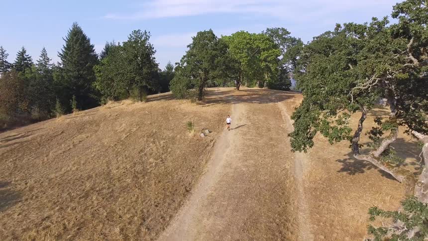 A jogger running down a dirt path in a woodland during the day