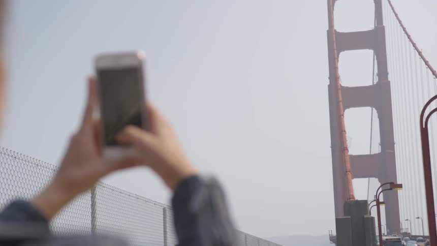 A woman takes a photo of the golden gate bridge on a windy day