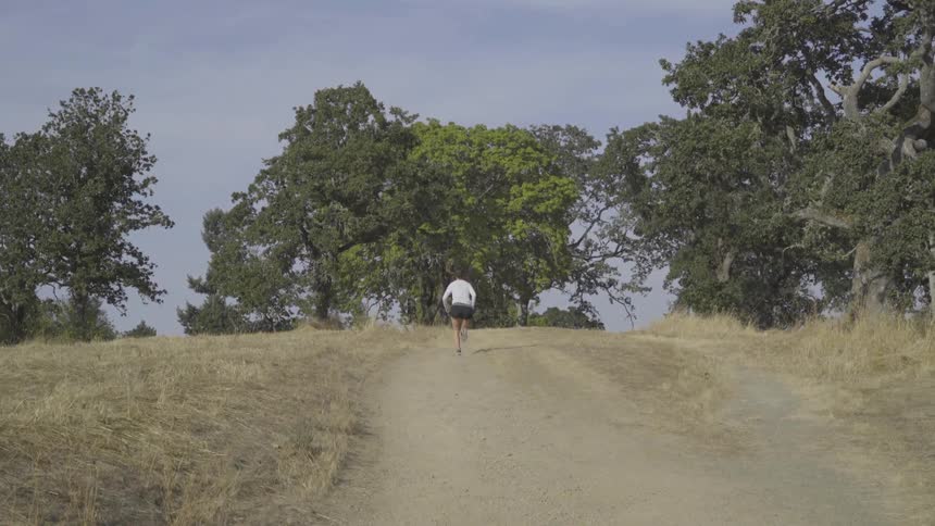 Woman runs along dirt road up hill toward trees