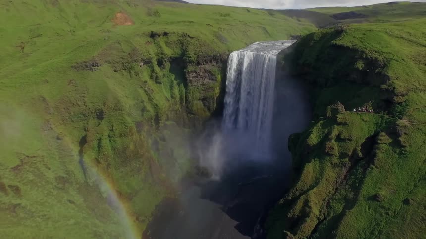 Double rainbow at the bottom of a waterfall surrounded by green mountains