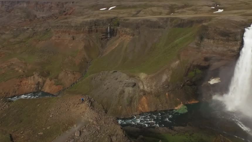 Person walking along a cliff ledge near a waterfall