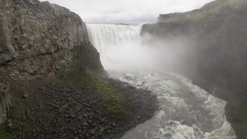A waterfall and the river is raging down a narrow canyon creating a mist