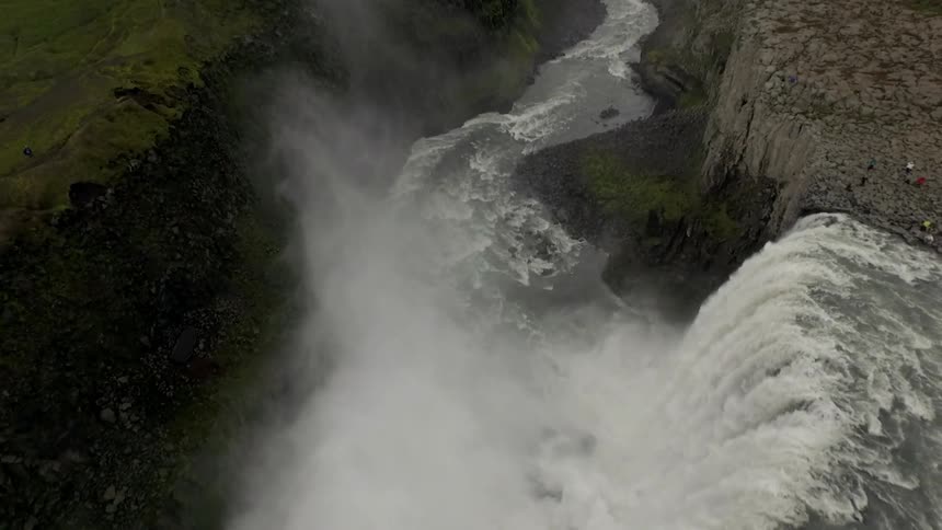 Aerial view of a waterfall crashing into a river and water spraying into the air between steep banks