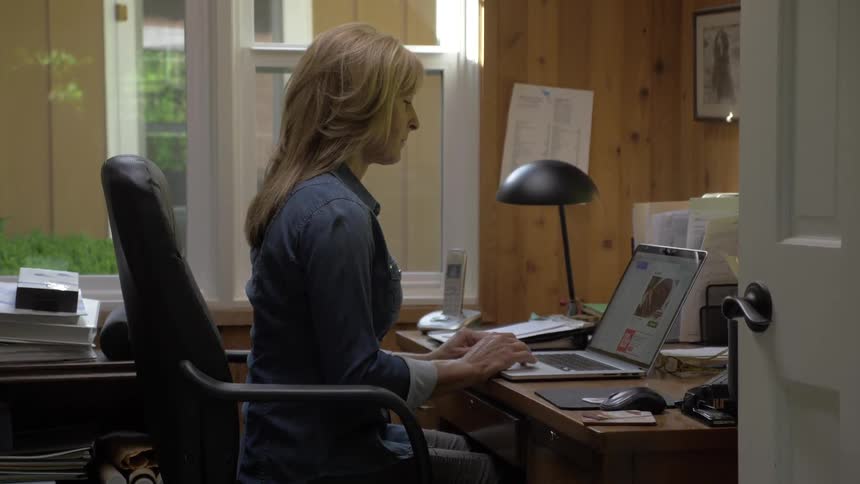 A woman sits at a desk using a laptop in a home office