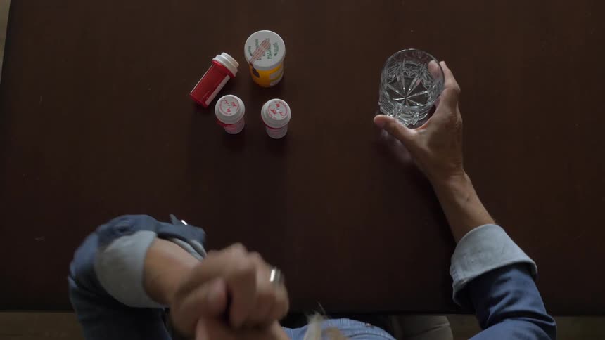 A woman takes a pill out of a bottle and takes it with some water
