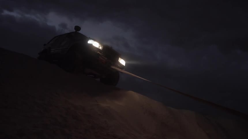 An suv is stuck in sand and pulled by rope over a dune