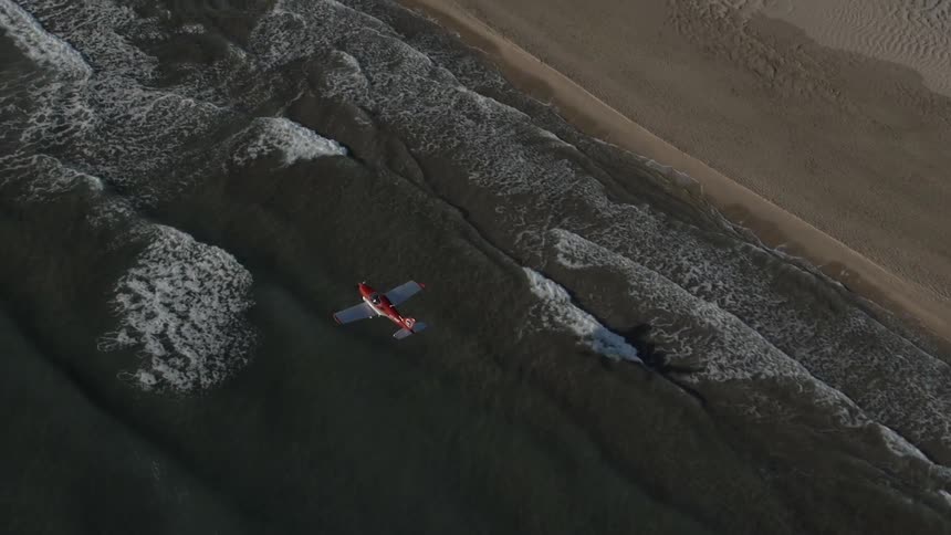 A small plane flies at a low elevation over the shoreline