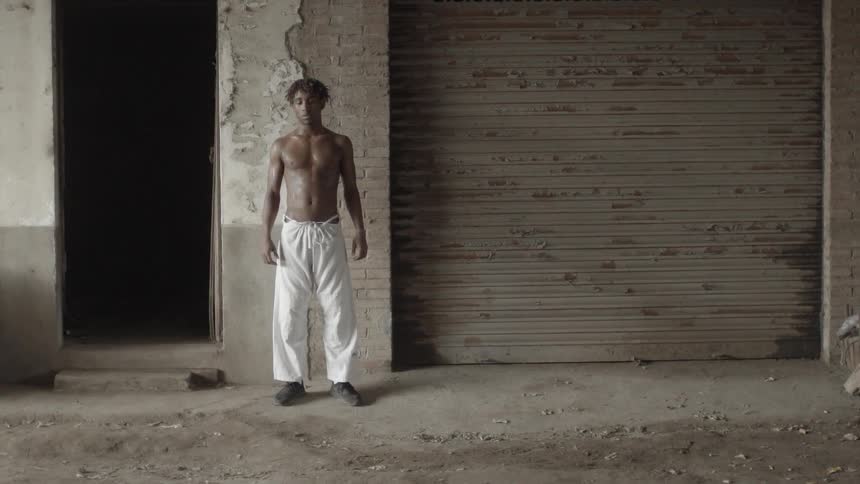 Shirtless man standing still outside of a building