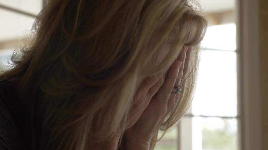 Blonde woman closes face with hands indoors during daylight