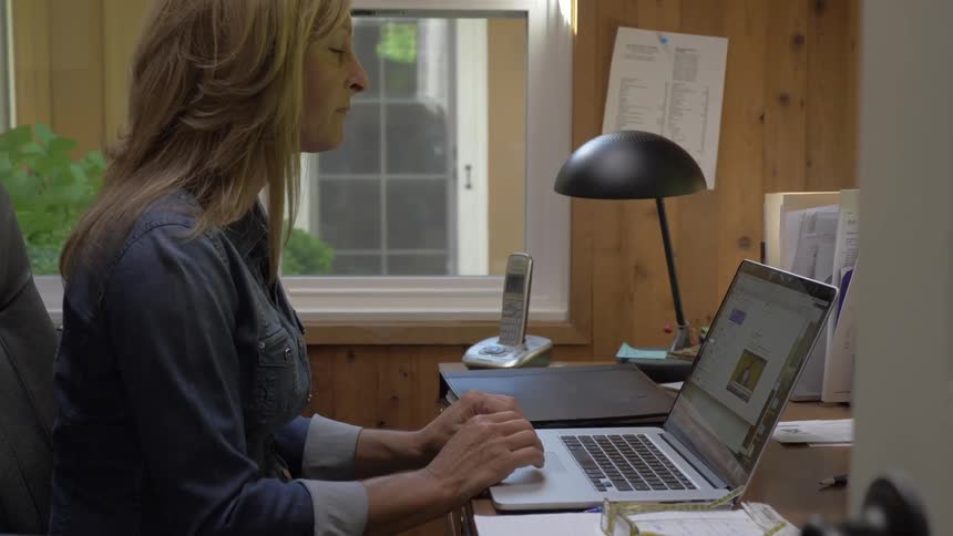 Blonde woman sits at the table uses laptop in the office during daylight