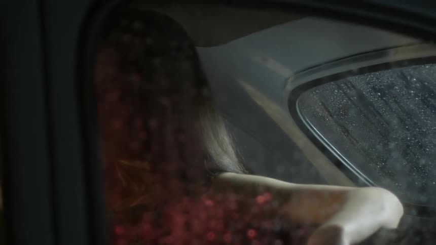 A woman sitting in the back seat of a car is illuminated by passing headlights