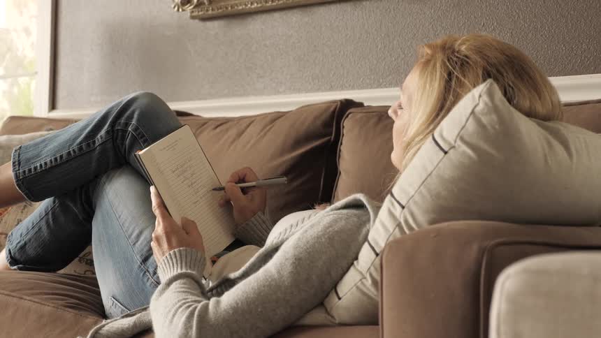 A woman laying on the couch writes in a notebook