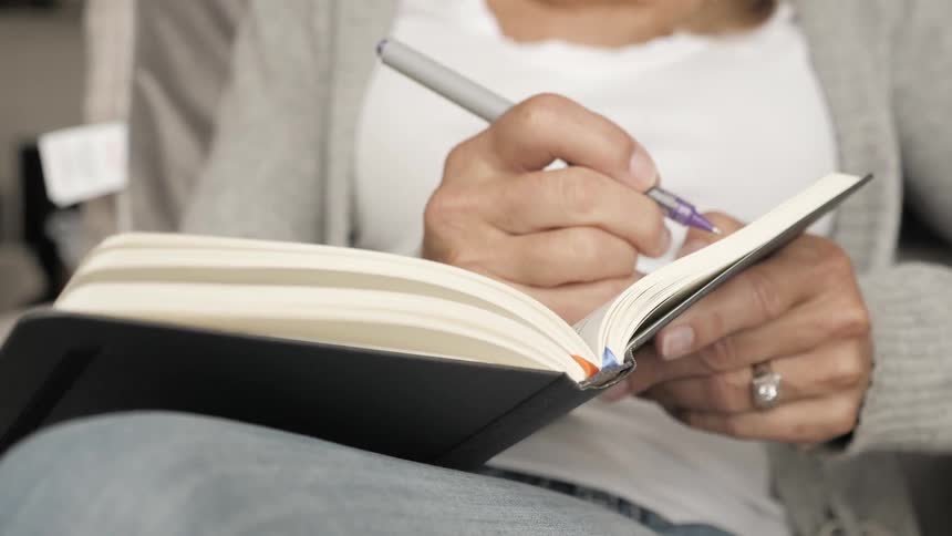 A woman flips pages and writes in a notebook