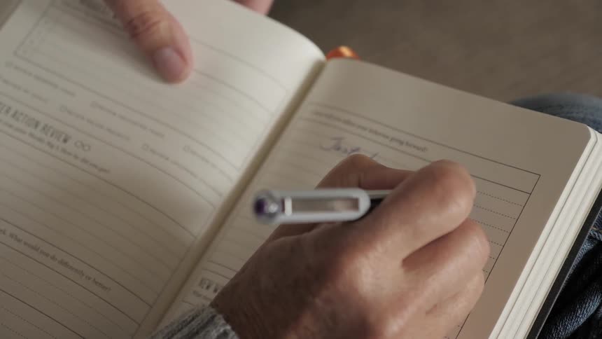 A person is writing in a workbook with a pen