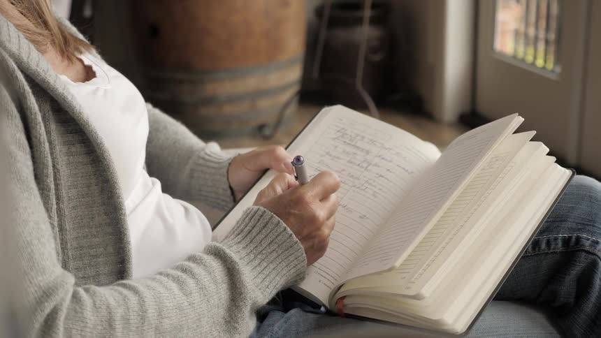 A woman is sitting in her home writing in a notebook