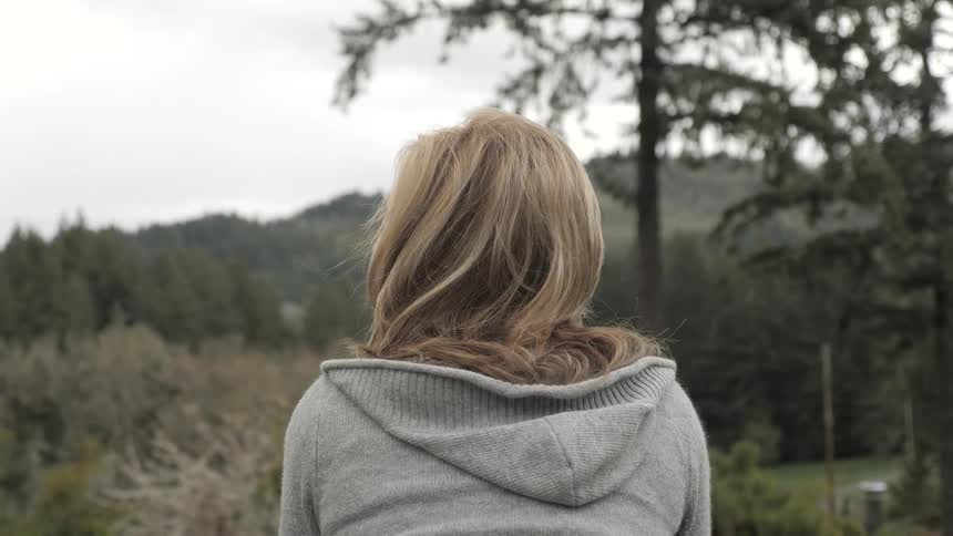 A female caucasian outside facing trees and bushes