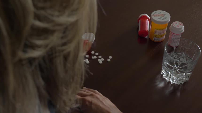 White person sits at a table looking at various medications